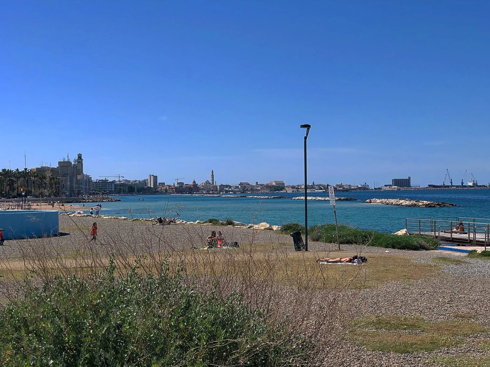 La spiaggia urbana di Pane e Pomodoro a Bari con il mare azzurro, i frangiflutti e il profilo della città sullo sfondo