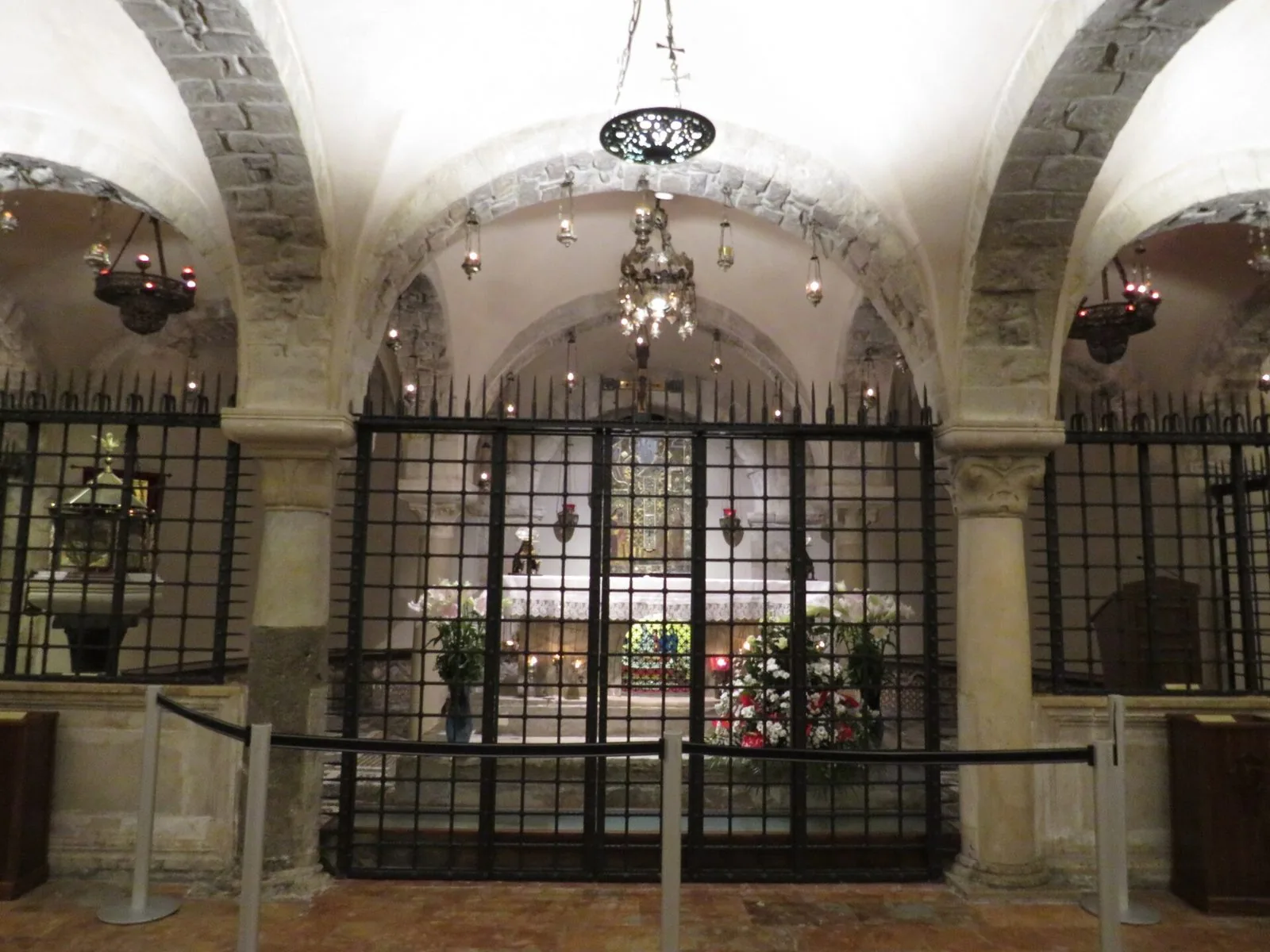 La cripta della Basilica di San Nicola a Bari con gli archi in pietra, le lampade votive e la cancellata davanti all'altare delle reliquie del santo